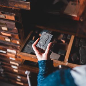 A hand holding a letterpress block above a type case — photo by Erik Mclean on Pexels
