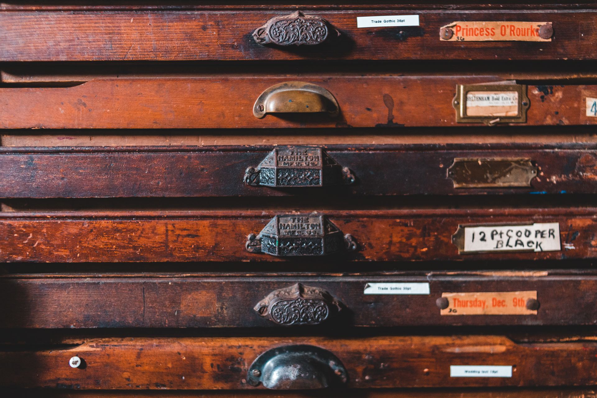 Vintage brown wooden cabinet with thin drawers decorated with cozy creative handles of different shape in craftsmanship