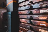 Weathered retro wooden cabinet with thin drawers decorated with creative handles of different shapes placed near old furniture in craftsmanship