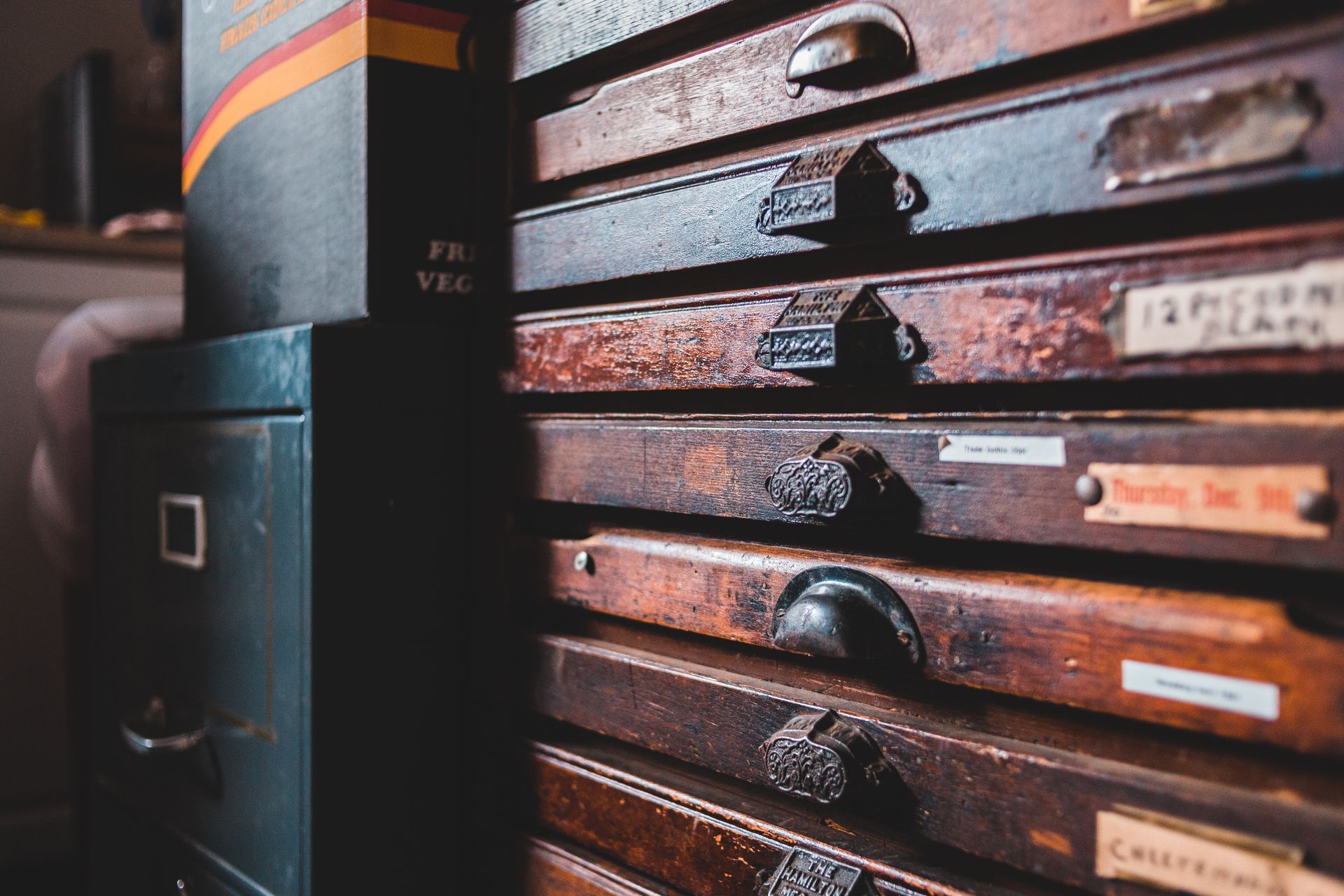 Weathered retro wooden cabinet with thin drawers decorated with creative handles of different shapes placed near old furniture in craftsmanship