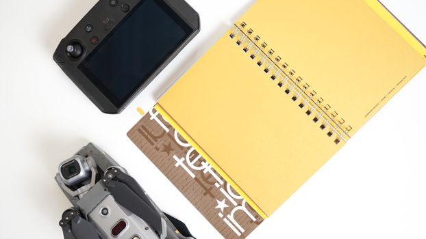 Overhead view of a drone controller and yellow notepad on a white surface, emphasizing modern technology.