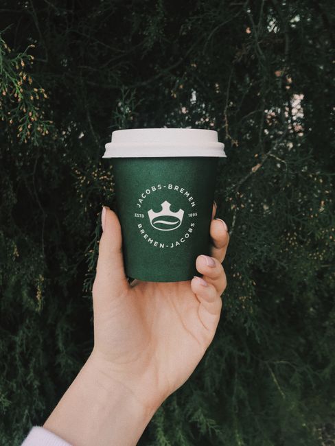 Crop anonymous female holding black paper cup of aromatic coffee to go against evergreen tree in park