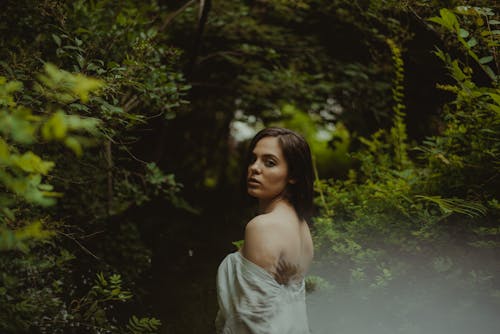 A Woman in White Off-Shoulder Dress Standing Near Green Plants