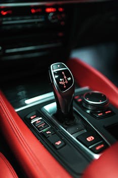 Close-up view of a modern car's gear shifter with red leather interior emphasizing luxury and technology.