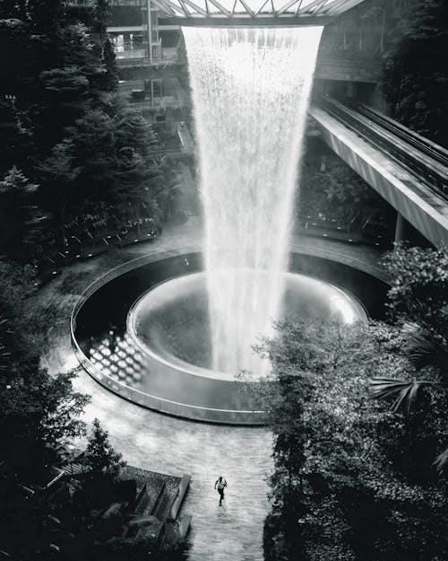 From above of black and white distant anonymous person running in amazing Singapore Changi Airport near massive water fountain and lush foliage