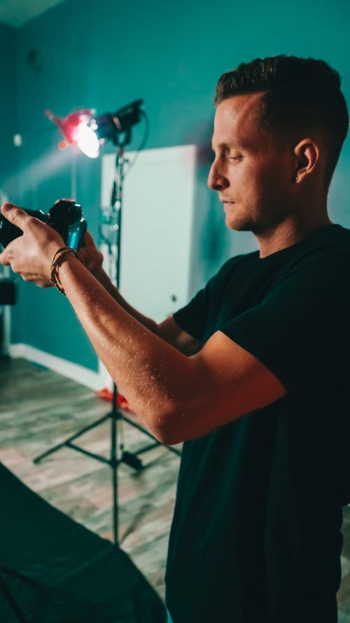 Free Side view of serious young male photographer in t shirt setting up professional camera during shooting in modern studio Stock Photo