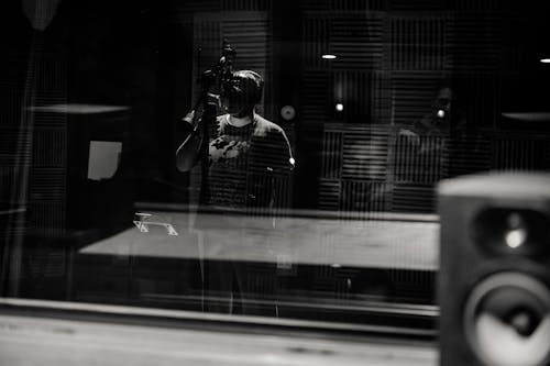 Free Through glass of black and white anonymous male musician in headphones singing with microphone while recording song in modern studio Stock Photo
