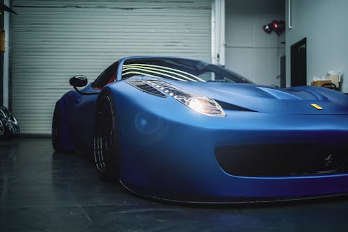 Luxury low electric blue sports car with glowing headlights parked in grungy workshop