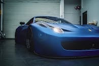 Luxury low electric blue sports car with glowing headlights parked in grungy workshop