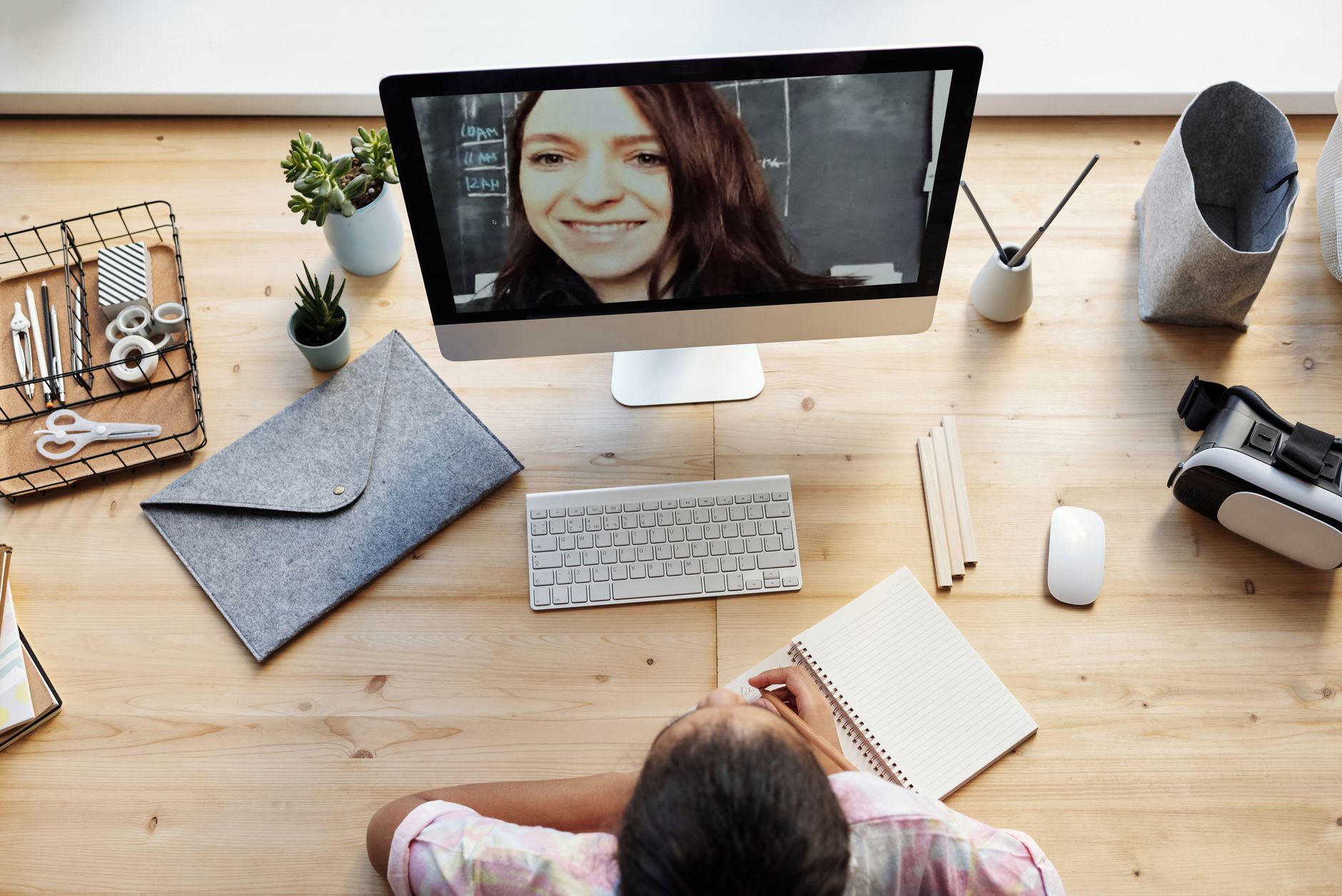 Vista cenital de una mujer en videoconferencia con otra mujer que aparece en la pantalla de un ordenador de sobremesa