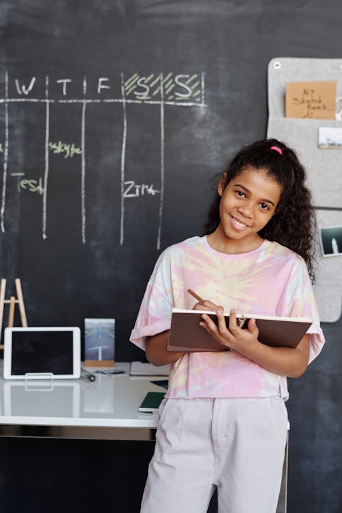 Girl in Pink and White Crew Neck T-shirt Holding Brown Notebook