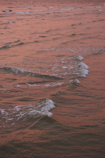 From above of foamy waves of picturesque sea reflecting pink sky color during bright sunset