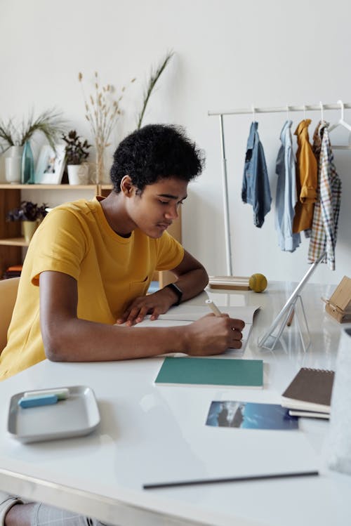 Free Boy Wearing Yellow Shirt While Writing on White Paper Stock Photo