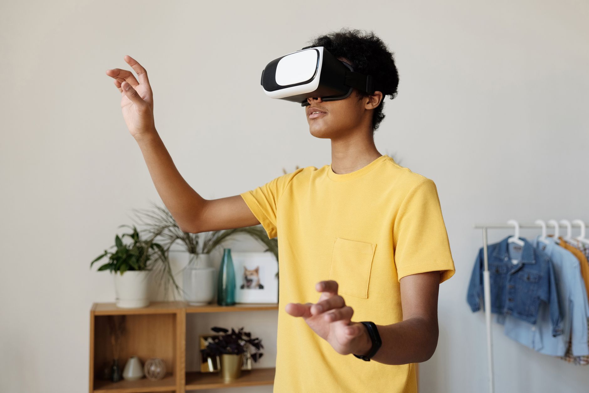 Teenage boy interacting with VR headset indoors, enjoying virtual experience.
