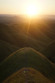 Beautiful sunrise over rolling hills with sunbeams illuminating the landscape.