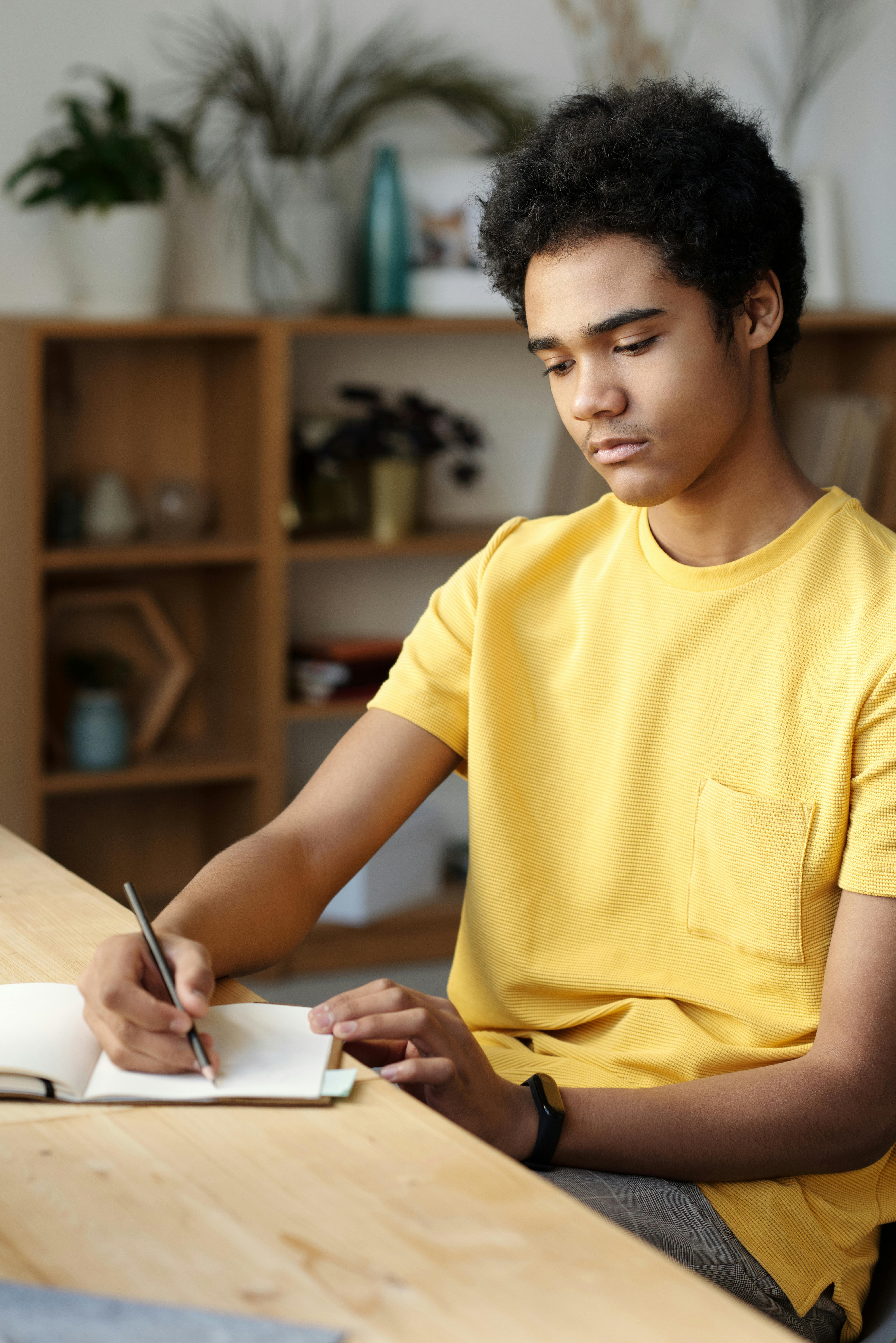 man in yellow crew neck t shirt writing on white paper