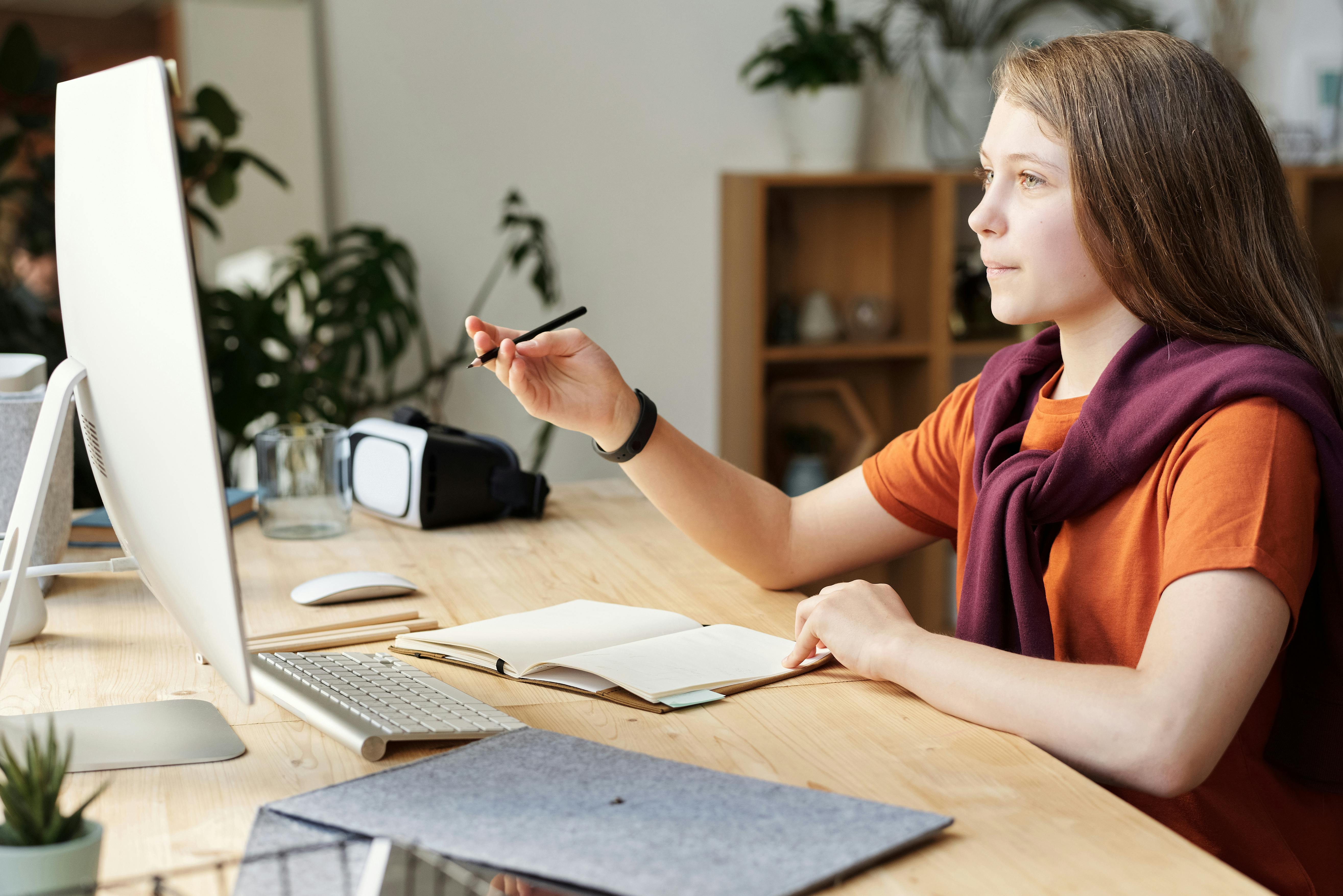 girl holding pencil while looking at imac