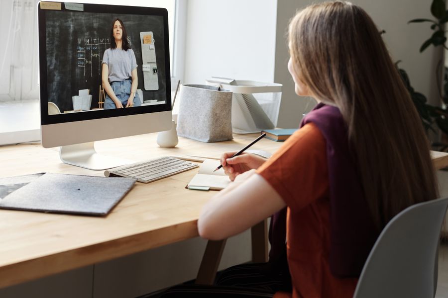 Teen girl attending an online class at home, takes notes at her desk.