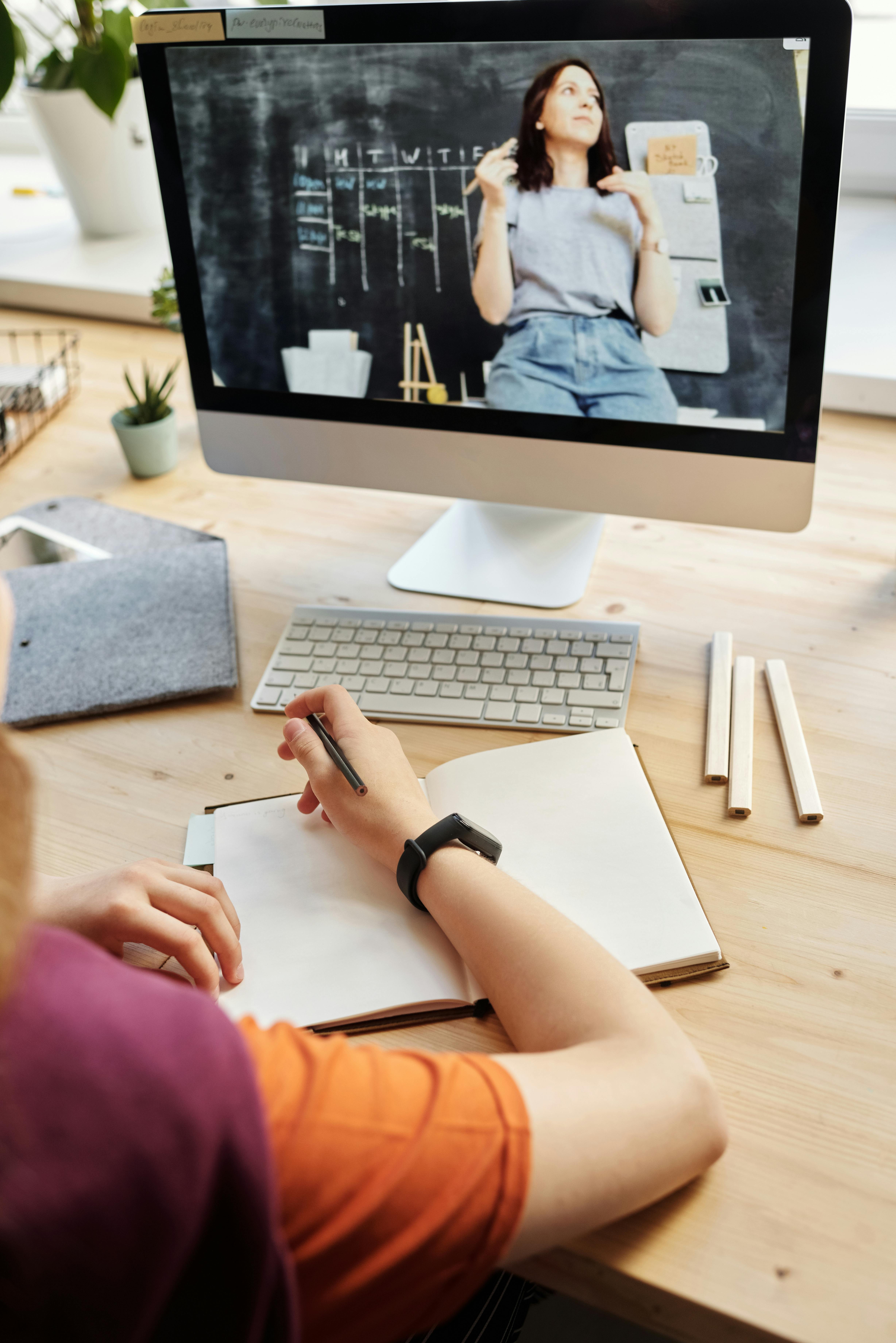 person using silver imac while holding pencil