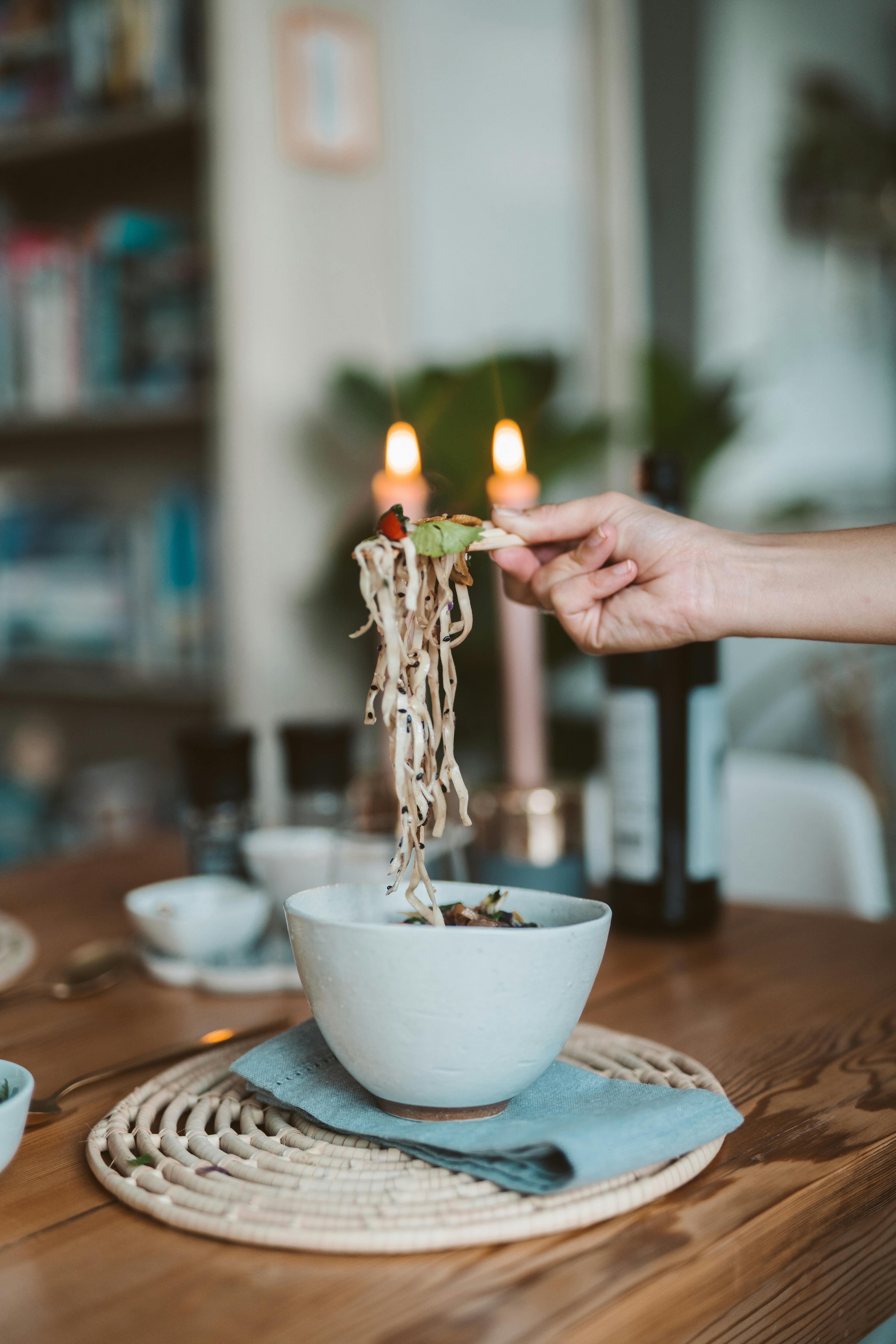 A cozy meal with Asian noodles and candlelight ambiance on a wooden dining table.
