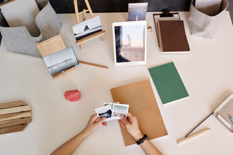 Hands arranging instant photos on a tidy desk with tablet and notebooks.
