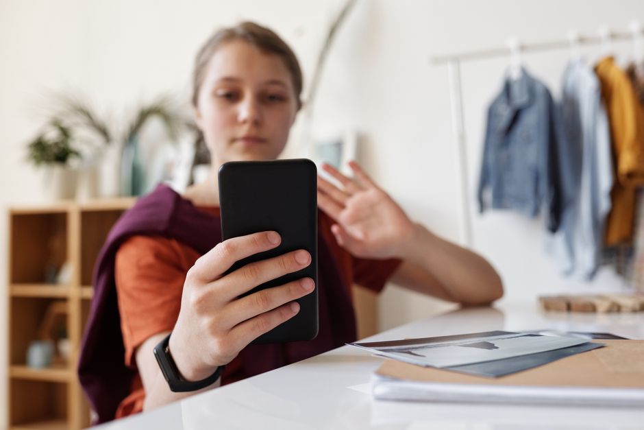 Teenager-Mädchen lächelt und winkt während eines Videoanrufs mit Smartphone drinnen.