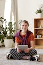 一个快乐的青少年坐在地板上，用着平板电脑，家里满是植物