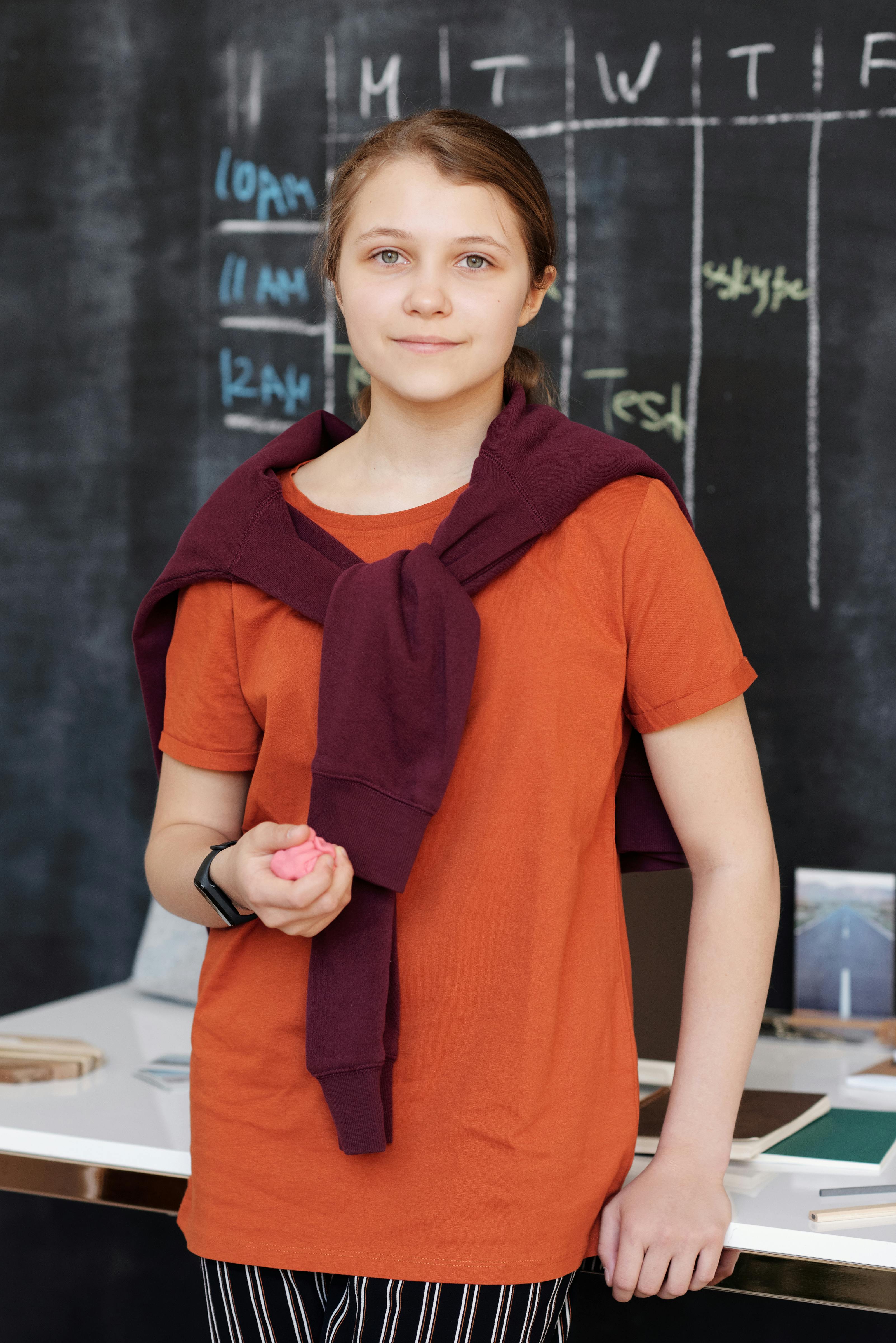 girl in orange shirt smiling while holding pink kinetic sand