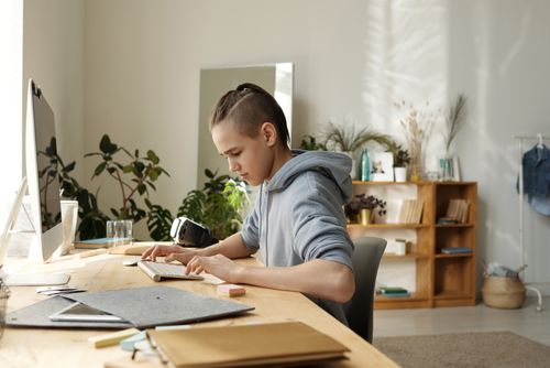 Free Teenager focused on study at home desk with computer and books in light-filled room. Stock Photo