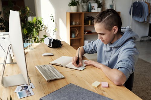 Free Boy in Gray Hoodie While Writing on His Notebook Stock Photo