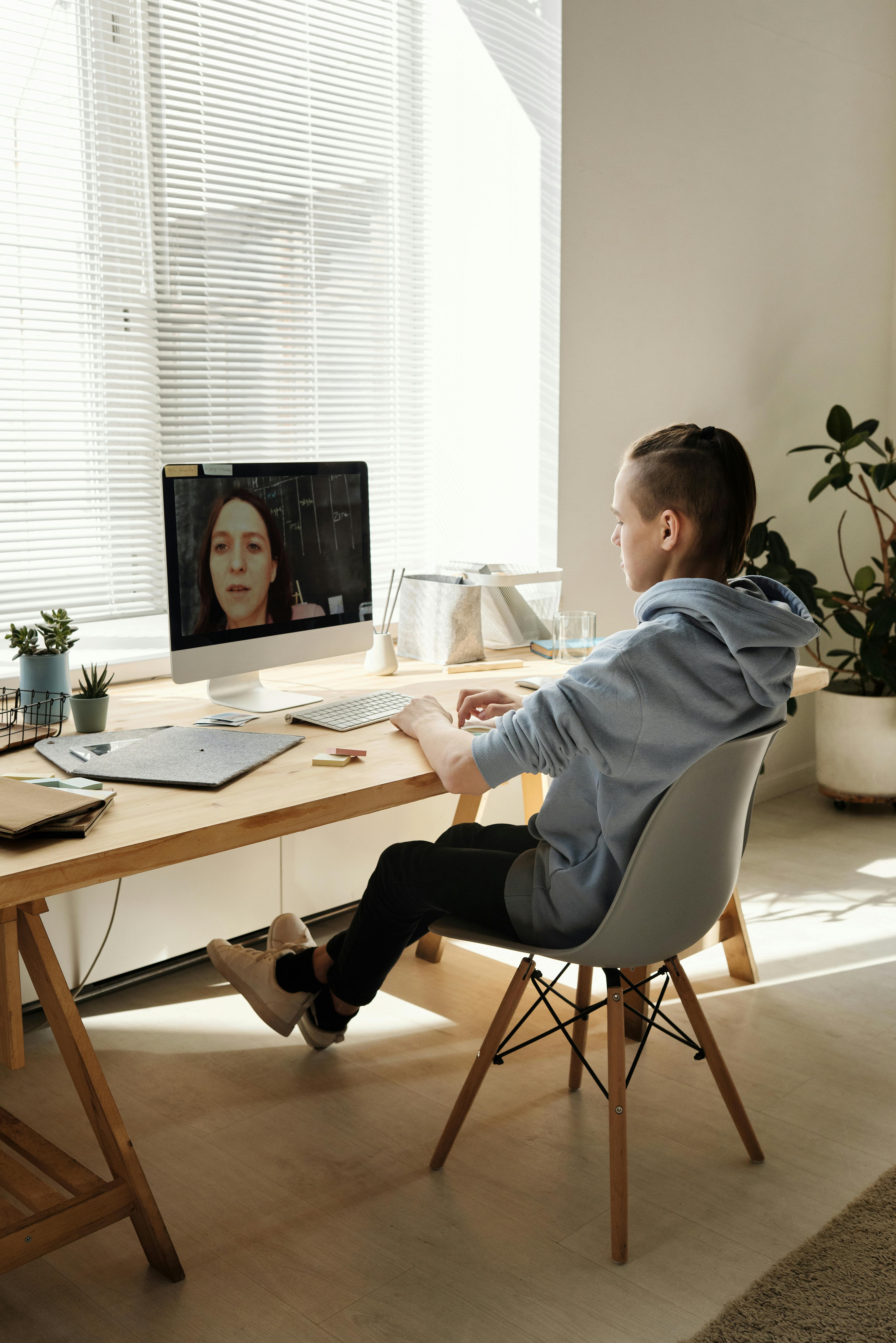 photo of boy sitting on chair while looking at the imac