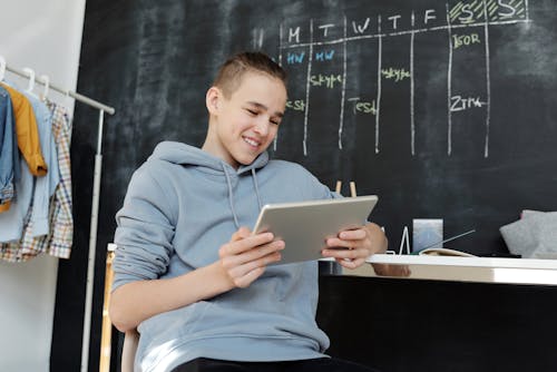 A Boy in Gray Hoodie Using His Tablet
