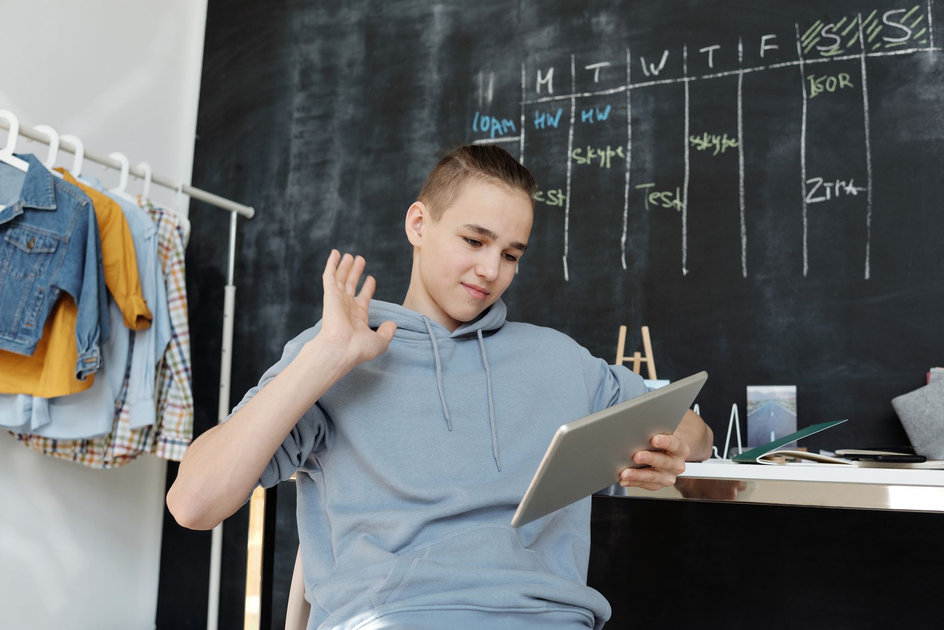 線上課程沒人報名?3種預熱行銷策略快速提升銷售 A teenager uses a tablet for online learning in a cozy home setting, waving at the screen.