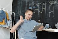 一名青少年在舒适的家庭环境中，对着屏幕挥手，使用平板电脑进行在线学习