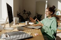 一名妇女穿着绿色连帽衫，正在家庭办公桌前进行视频通话