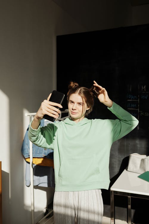 A Young Woman in a Green Hoodie Taking a Selfie