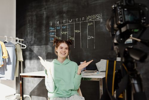 Free Young girl in a green hoodie smiling and gesturing during a video shoot in a creative home space. Stock Photo