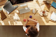 一个孩子在家里的办公桌前做手工，周围摆满了文具和电脑