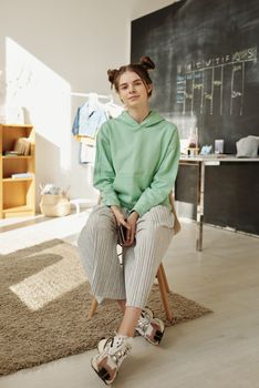 一位穿着绿色连帽衫的少女，坐在明亮现代房间的凳子上