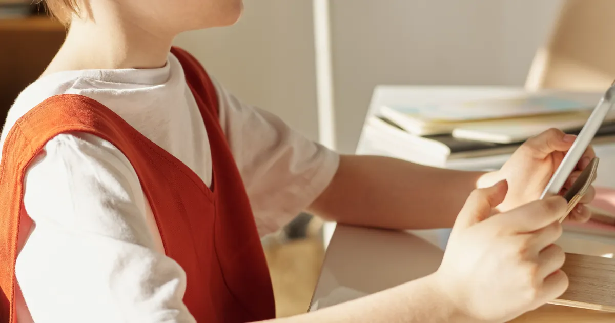 A boy in a red vest holding a tablet at a desk, seen close up, representing the documentation requirements under California SB 1119 Adam's Law