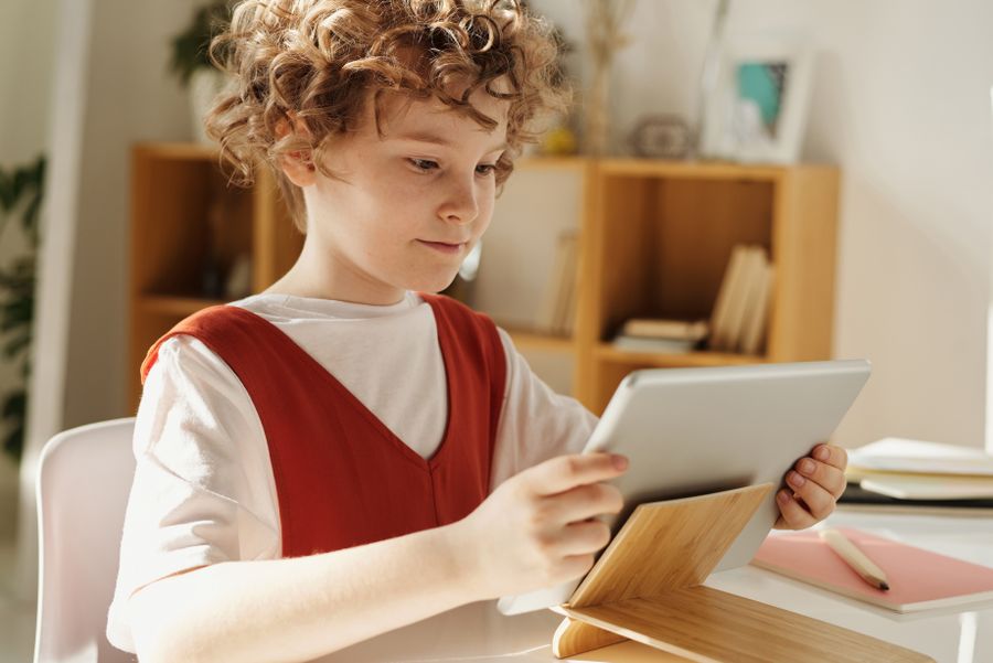 A school-age child using a tablet at a study desk