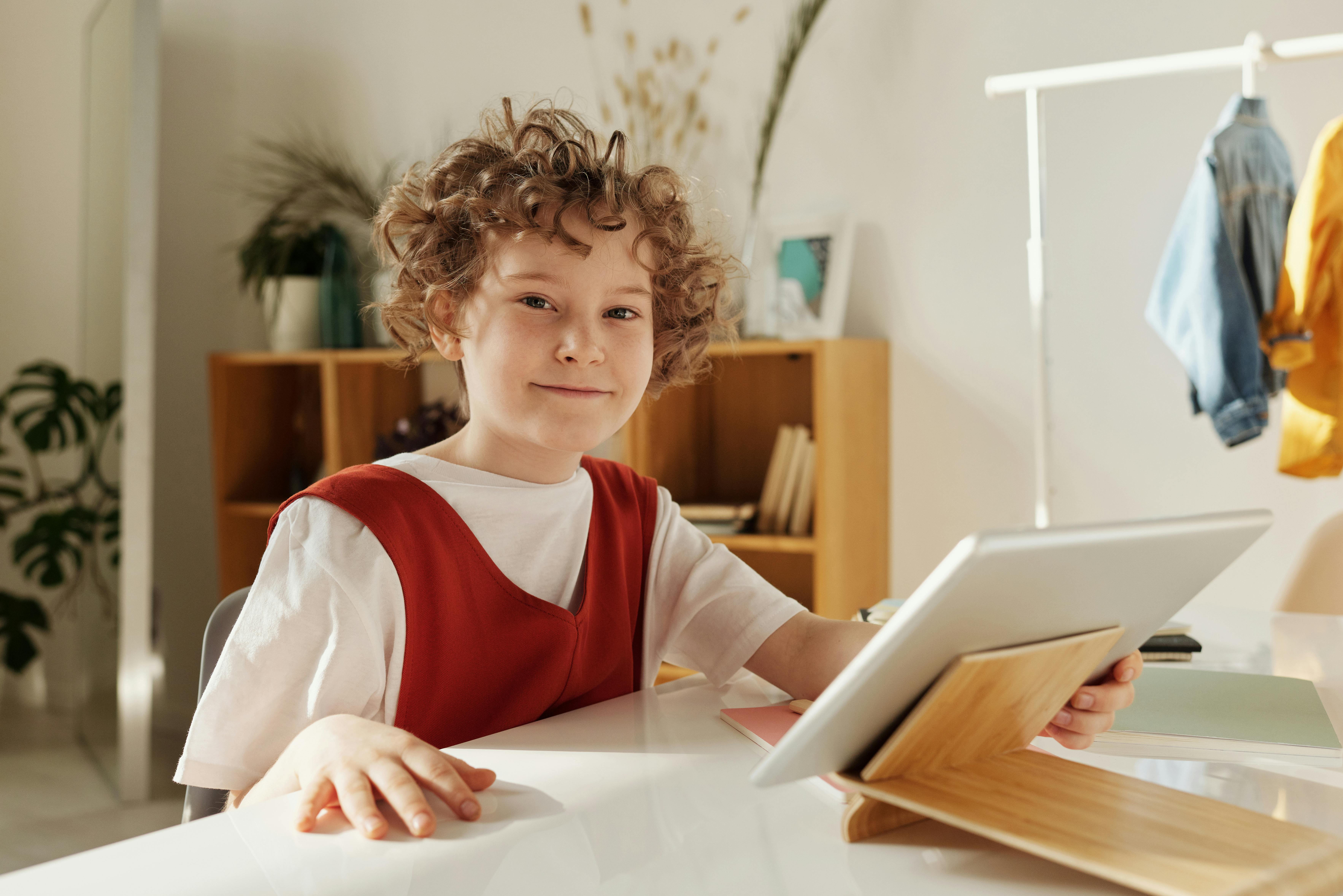 child smiling while holding silver tablet