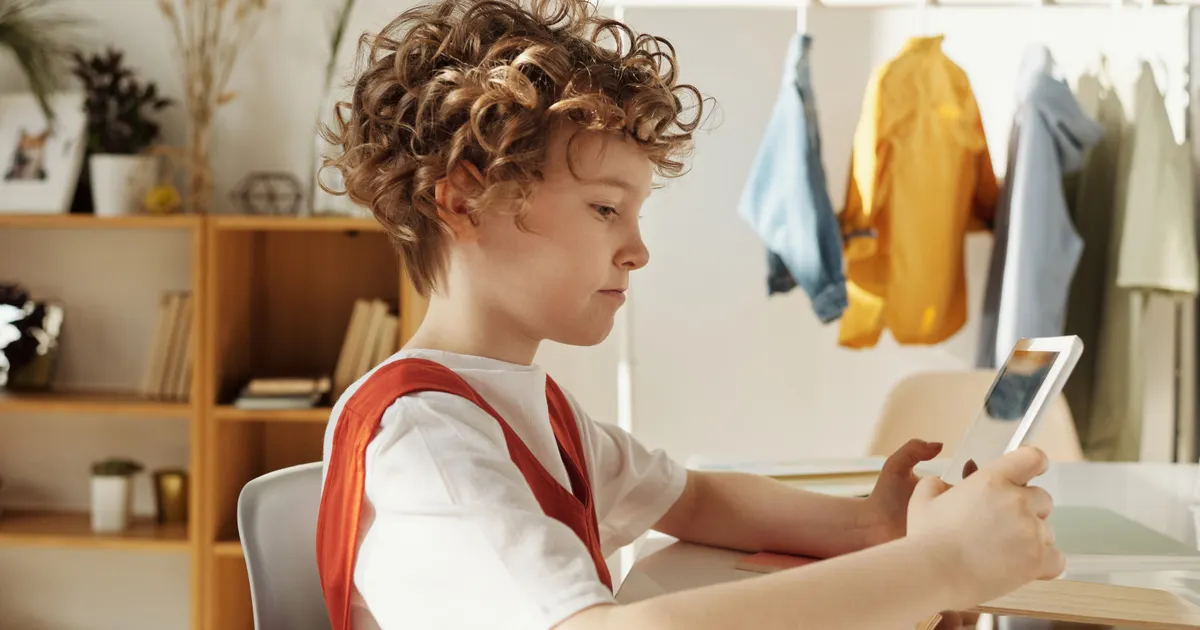 A boy in a red vest using a tablet at a desk in a bright room, representing regulatory analysis and policy review