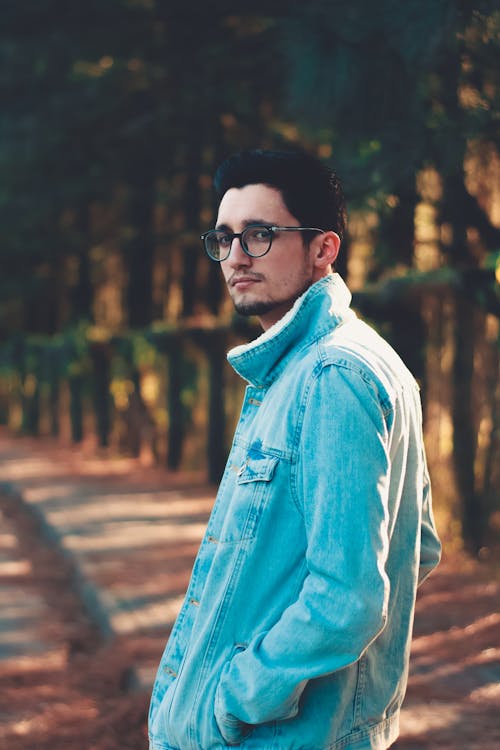 Side view of young man in denim jacket and eyeglasses standing in park