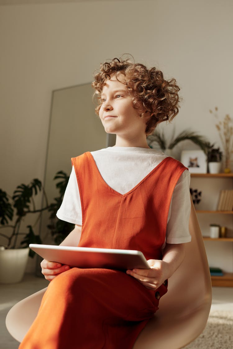 Photo Of Child Sitting On Chair While Holding Tablet