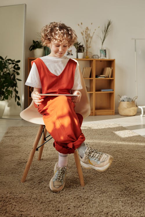 Photo of Child Sitting on Chair While Using Tablet