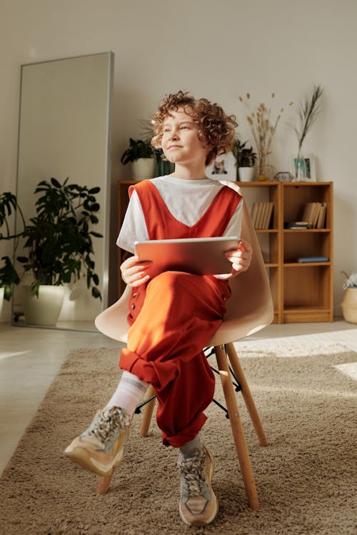 Free Photo of Child Sitting on Chair While Holding Tablet Stock Photo