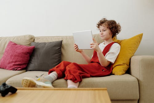 Photo of Child Sitting on Couch While Holding Tablet