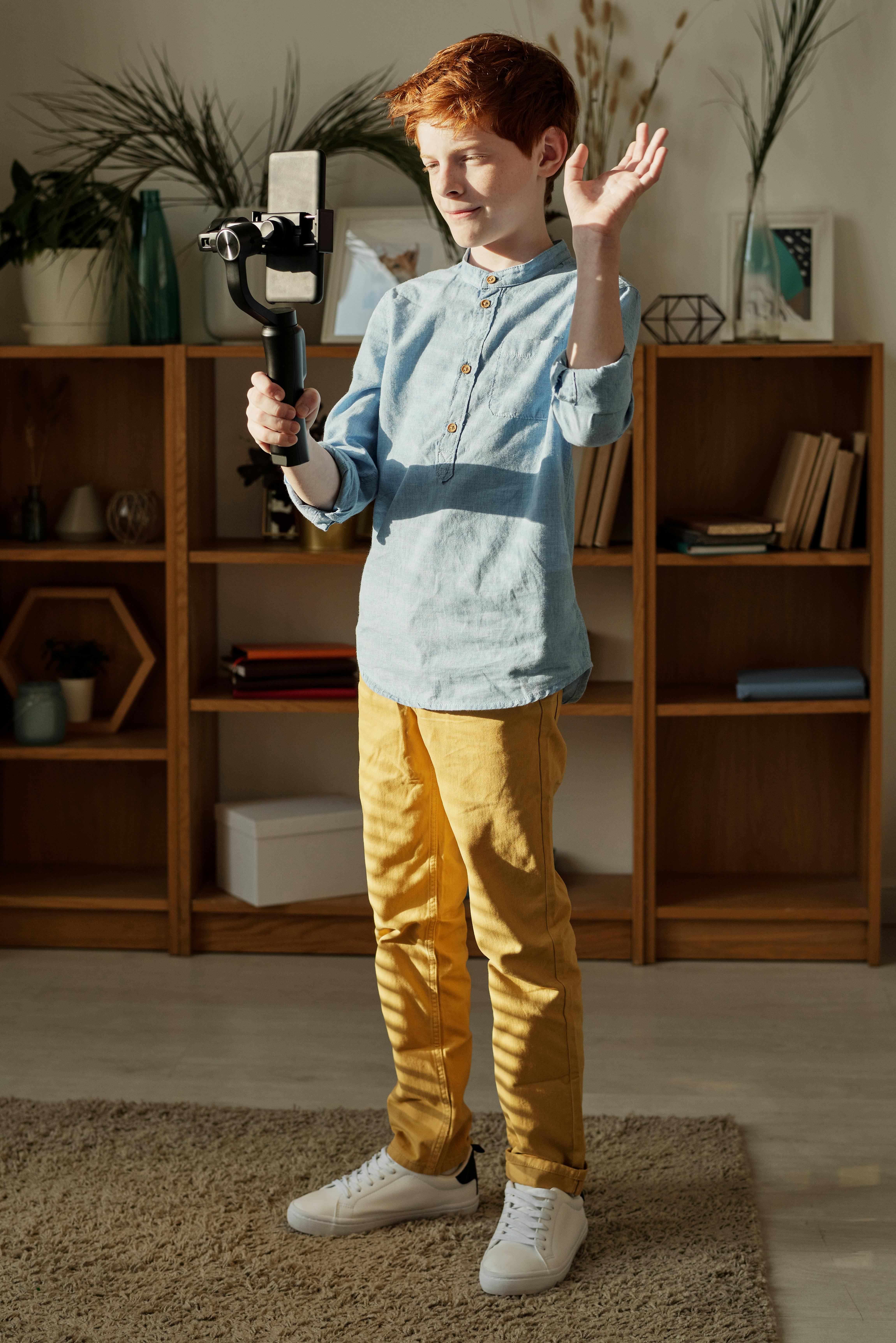 photo of boy standing while holding black selfie stick