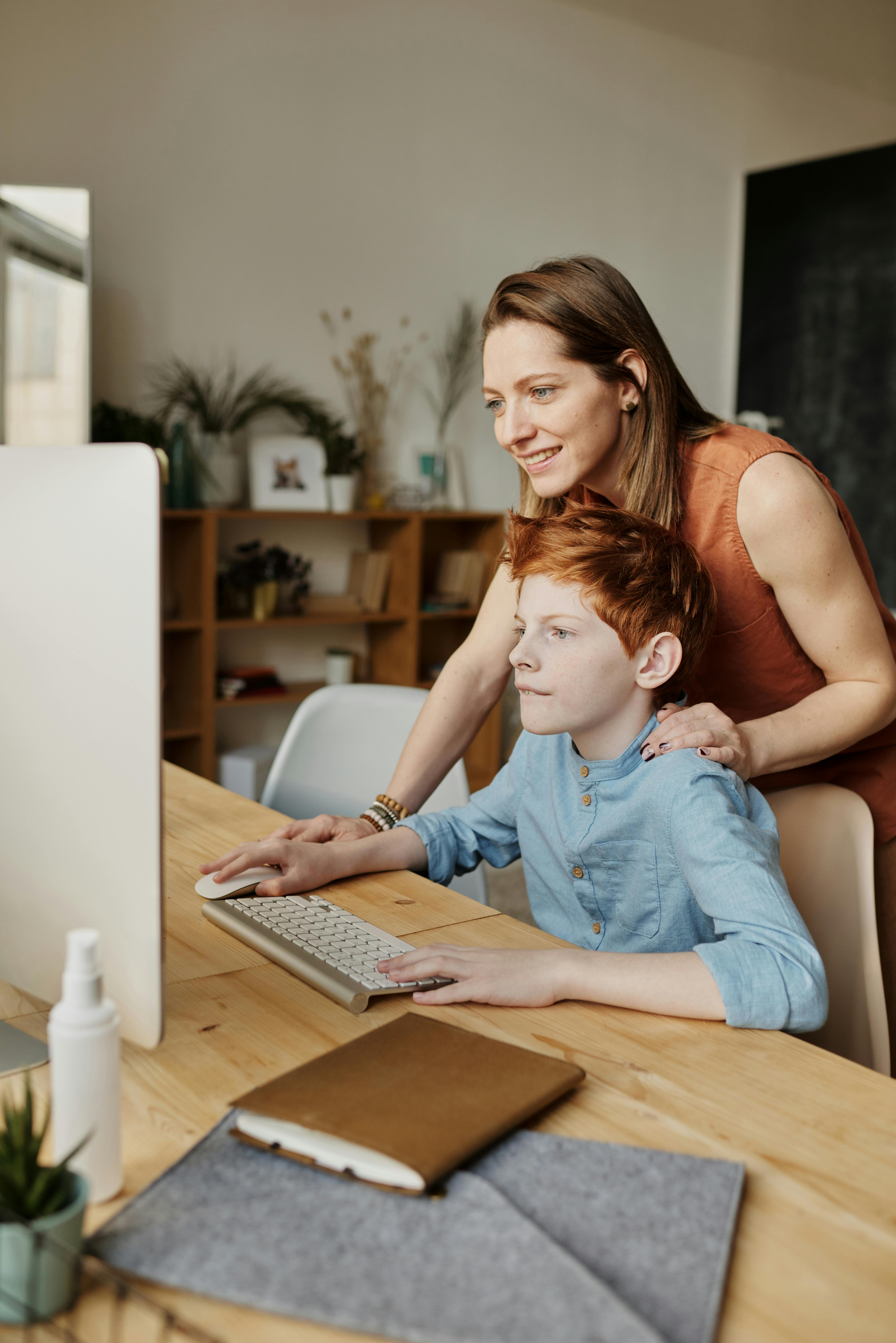 photo of woman and boy looking at imac